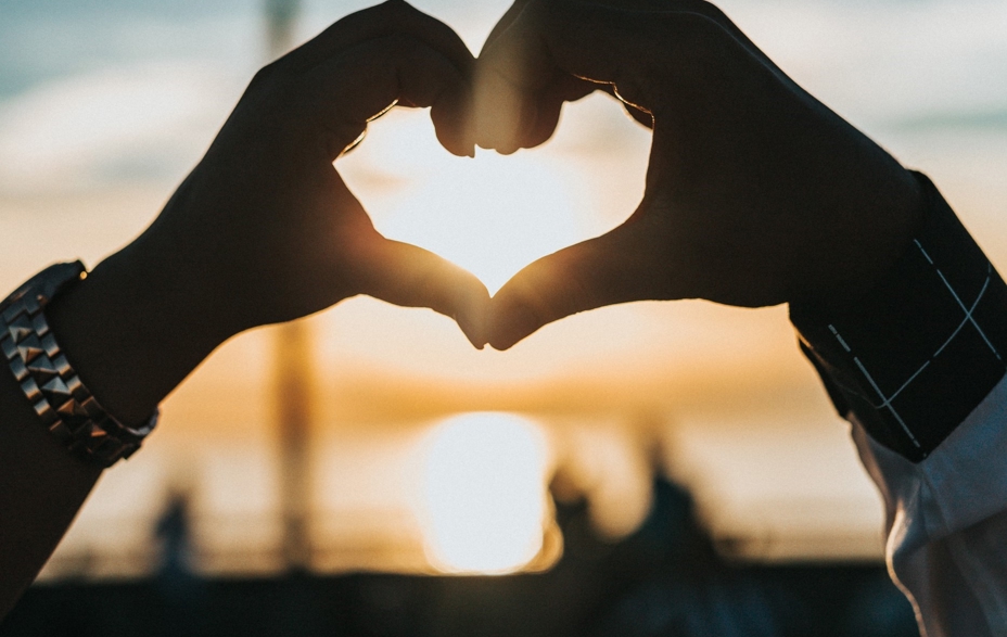 Hands shaped as a heart with a sunset in the background