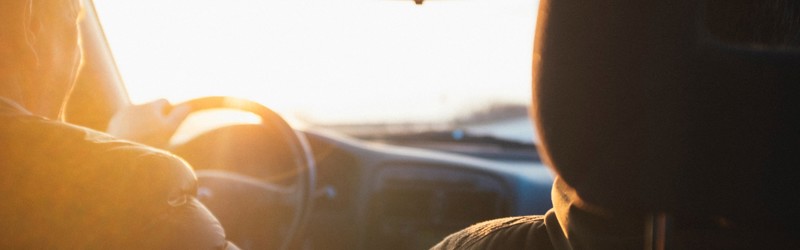 Two people driving a car into the sunrise