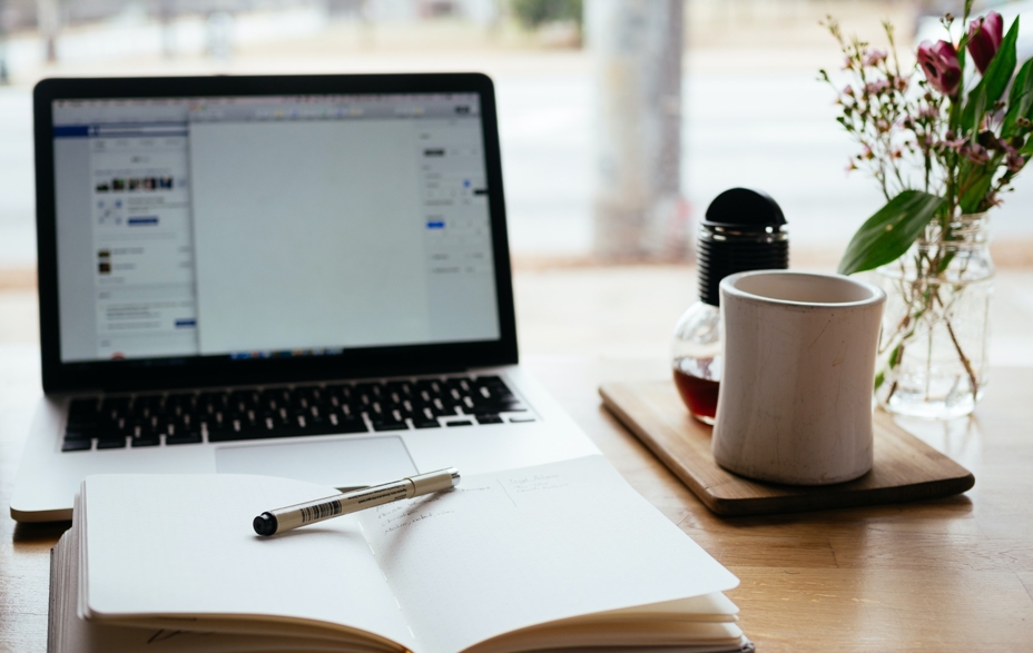 Desk with computer, open book and a coffee cup