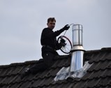 Skorstensfejer sidder på taget og renser en skorsten