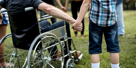 Billedet viser en kørestolsbruger, der holder et barn i hånden